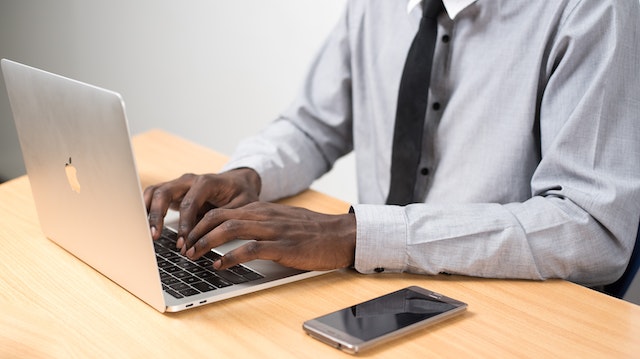 person wearing a black tie working on their laptop with their phone next to them on a desk